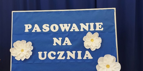 Powiększ grafikę: tablica umieszczona na środku auli z napisem pasowanie na ucznia.