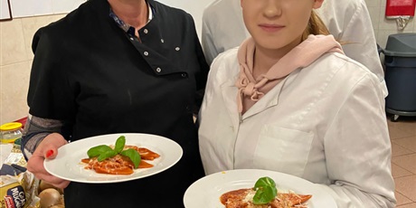 Powiększ grafikę: Na fotografi uczniowie stoją z nauczycielem i prezentują dania kuchni włoskiej.